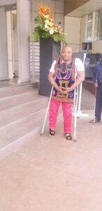 Sunday Ghali in a traditional regalia, standing with two crutches under his arms.