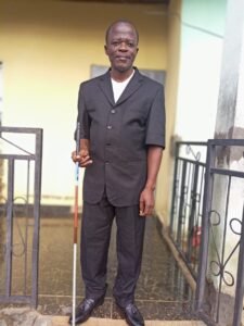 Samuel Nyuincho in black suit, holding his white cane