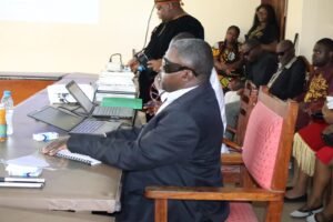 Ngong Peter Tonain, a visually impaired scholar, sits at a presentation table with laptops and a Braille manuscript as he defends his PhD thesis before a seated audience in the Boardroom of the Faculty of Social and Management Sciences, University of Buea, February 13, 2026